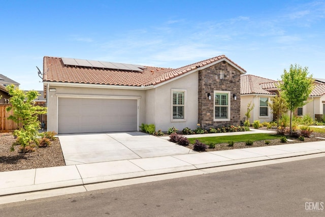 mediterranean / spanish home featuring an attached garage, stone siding, stucco siding, roof mounted solar panels, and a tiled roof