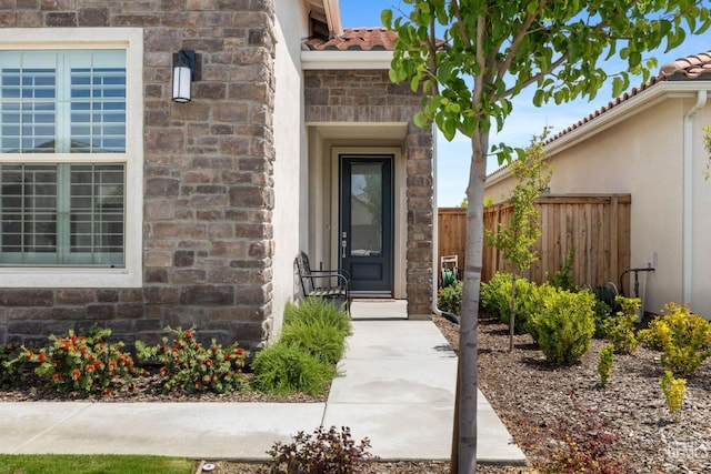 entrance to property featuring stucco siding, fence, stone siding, and a tile roof