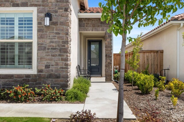 3308 Whispering Brook Ln, Shafter, CA 93263 - property entrance with stucco siding, fence, stone siding, and a tile roof