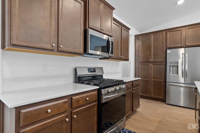 kitchen featuring dark brown cabinetry, appliances with stainless steel finishes, light countertops, light wood-type flooring, and vaulted ceiling
