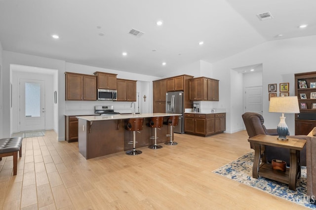 kitchen with visible vents, a breakfast bar, light wood-style flooring, appliances with stainless steel finishes, and vaulted ceiling