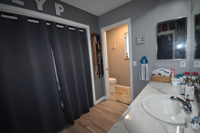 full bathroom with baseboards, toilet, a textured ceiling, wood finish floors, and a sink