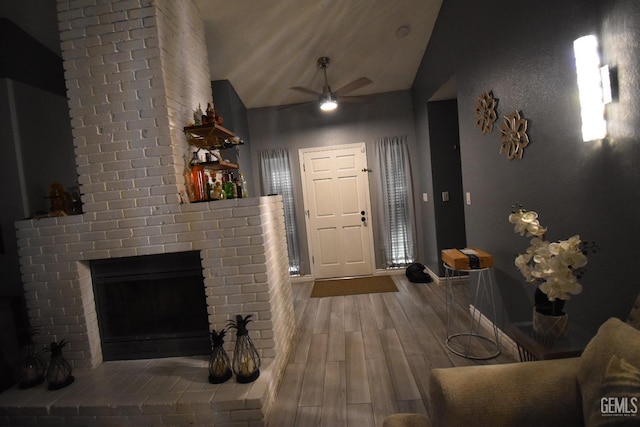 foyer with a brick fireplace, ceiling fan, vaulted ceiling, and wood finished floors