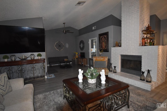 living area featuring lofted ceiling, visible vents, a fireplace, and wood finished floors