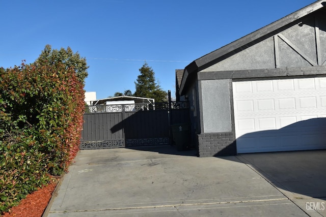 view of side of home with brick siding, stucco siding, a gate, fence, and a garage