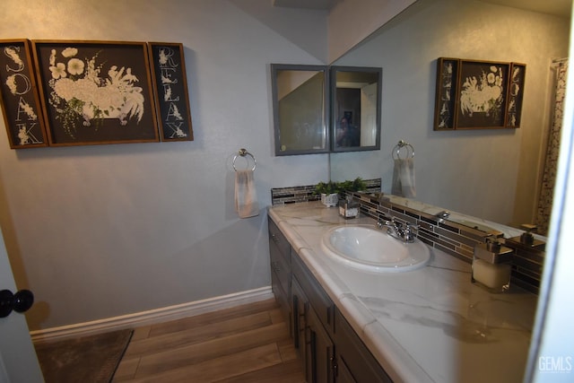 bathroom featuring tasteful backsplash, baseboards, wood finished floors, and vanity