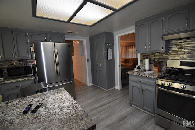 kitchen with stainless steel appliances, light wood-type flooring, decorative backsplash, and light stone countertops