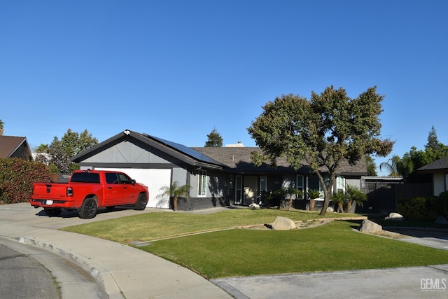 ranch-style house with an attached garage, roof mounted solar panels, a front lawn, and concrete driveway