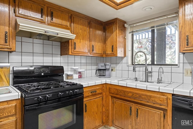 kitchen with brown cabinetry, decorative backsplash, under cabinet range hood, black appliances, and a sink