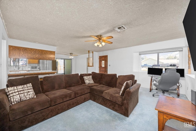 carpeted living area featuring a ceiling fan, a textured ceiling, visible vents, and a sink