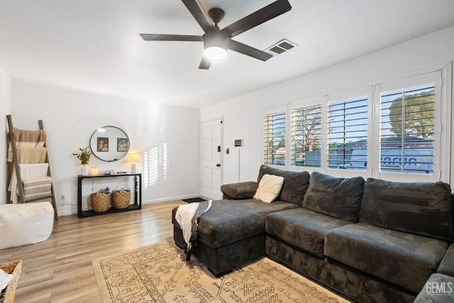 living area featuring baseboards, light wood-style flooring, visible vents, and a ceiling fan