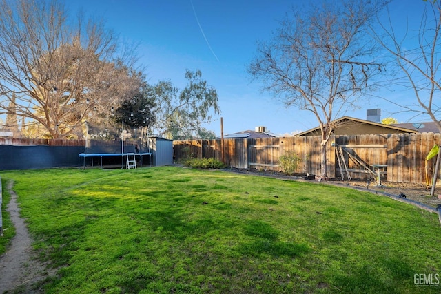 view of yard featuring a storage shed, a fenced backyard, a trampoline, and an outbuilding