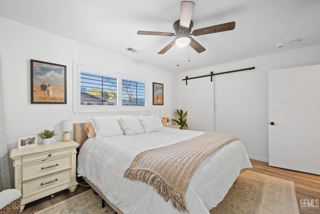 bedroom with a barn door, dark wood-style flooring, visible vents, and a ceiling fan