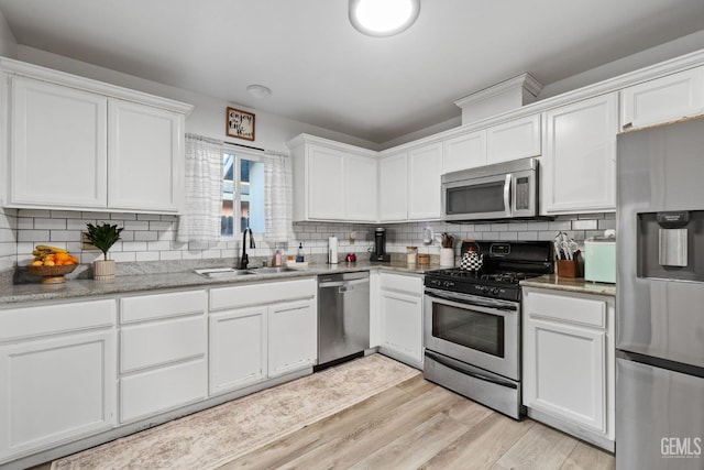 kitchen featuring stainless steel appliances, backsplash, light wood-style flooring, white cabinets, and a sink