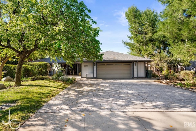 ranch-style home with a front lawn, decorative driveway, and an attached garage