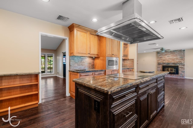 kitchen featuring dark brown cabinets, stainless steel microwave, island exhaust hood, and visible vents