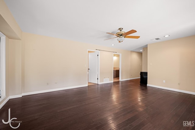 spare room featuring dark wood finished floors, visible vents, a barn door, a ceiling fan, and baseboards