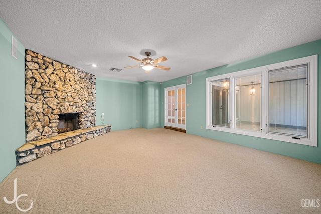 unfurnished living room featuring carpet, a fireplace, visible vents, a ceiling fan, and a textured ceiling