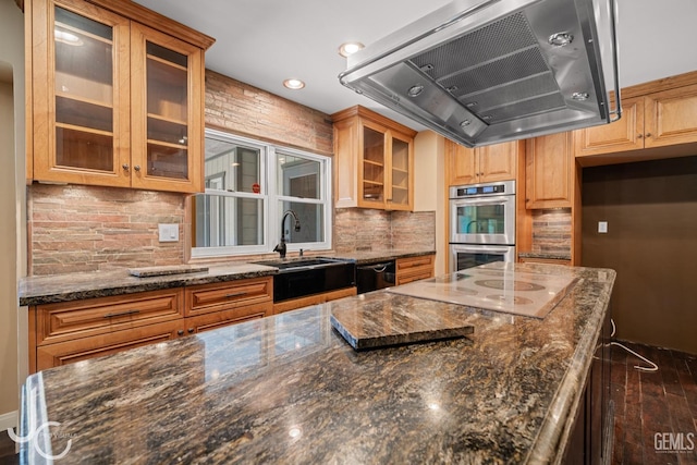 kitchen with a sink, wall chimney exhaust hood, dark stone countertops, and stainless steel double oven