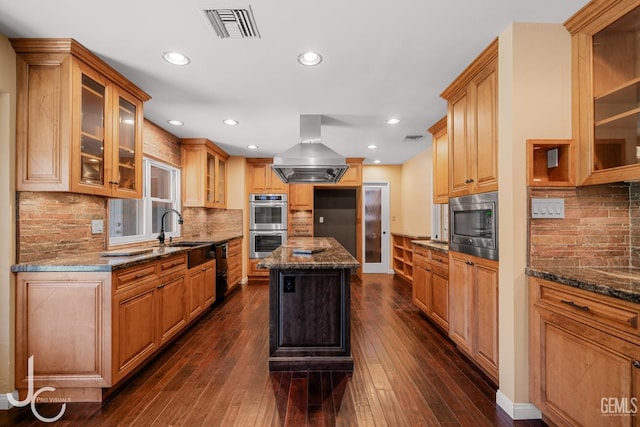 kitchen featuring a sink, visible vents, ventilation hood, a center island, and glass insert cabinets