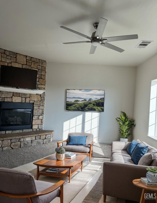 living room featuring ceiling fan and a stone fireplace