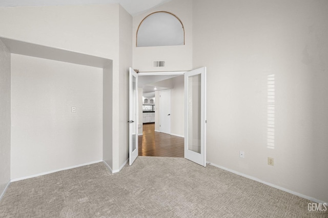 empty room featuring a high ceiling, carpet flooring, and french doors