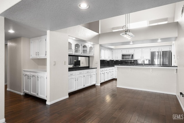 kitchen featuring pendant lighting, white cabinets, dark hardwood / wood-style flooring, kitchen peninsula, and stainless steel appliances