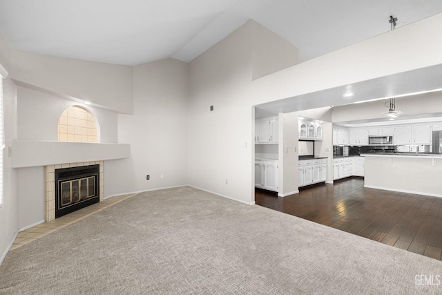 unfurnished living room with a tile fireplace, high vaulted ceiling, and dark hardwood / wood-style flooring