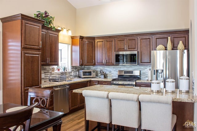 kitchen featuring a center island, light stone counters, backsplash, a kitchen bar, and appliances with stainless steel finishes