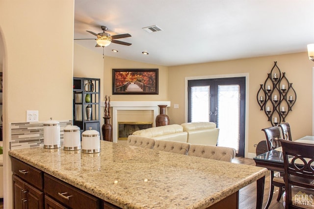 kitchen featuring light stone countertops, ceiling fan, lofted ceiling, dark brown cabinets, and hardwood / wood-style flooring