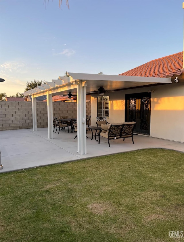 patio terrace at dusk featuring a yard, a pergola, and ceiling fan