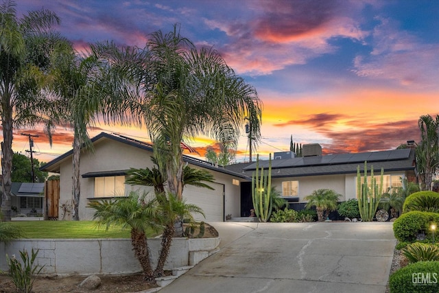 mid-century inspired home with a front lawn, concrete driveway, a garage, roof mounted solar panels, and stucco siding