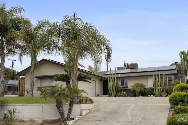 ranch-style house with solar panels, an attached garage, stucco siding, driveway, and a front yard