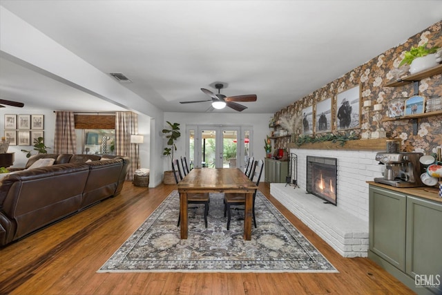 dining space with a fireplace, visible vents, ceiling fan, and french doors