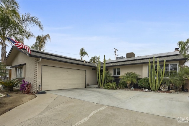 ranch-style home with an attached garage, driveway, roof mounted solar panels, and stucco siding
