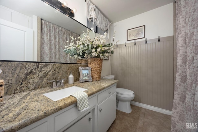 bathroom featuring tile patterned flooring, toilet, vanity, and wainscoting