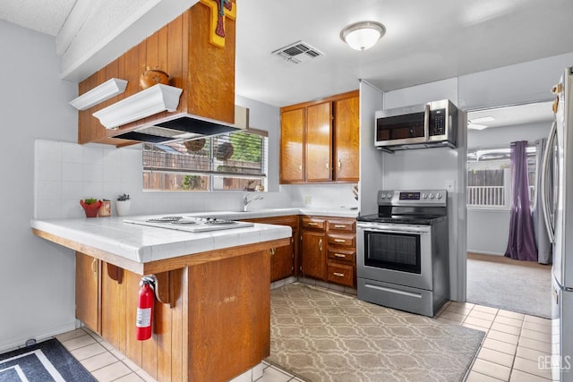 3406 Elm St, Bakersfield, CA 93301 - kitchen with tile counters, brown cabinets, a peninsula, appliances with stainless steel finishes, and visible vents