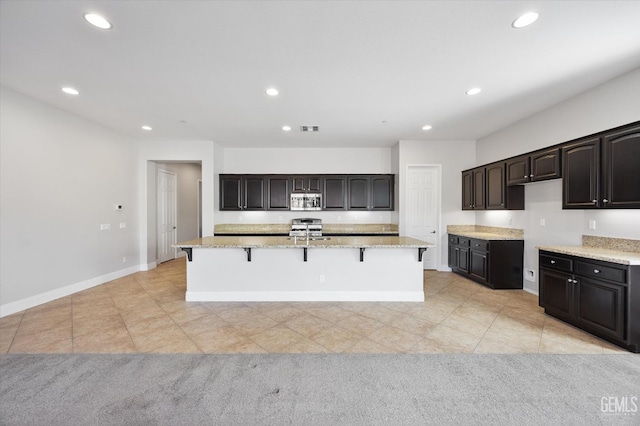 kitchen featuring light tile patterned flooring, stainless steel appliances, dark brown cabinets, and an island with sink