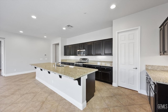 kitchen featuring light stone countertops, stainless steel appliances, sink, a kitchen breakfast bar, and a kitchen island with sink