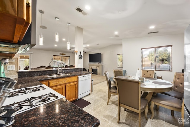 kitchen featuring white dishwasher, dark stone counters, lofted ceiling, pendant lighting, and sink