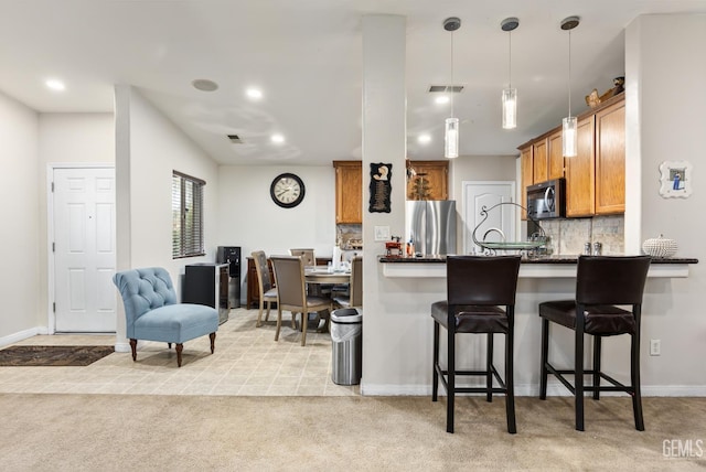 kitchen with stainless steel appliances, decorative light fixtures, light carpet, a kitchen bar, and kitchen peninsula