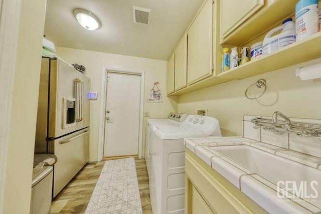 clothes washing area with washer and dryer, light hardwood / wood-style floors, and sink