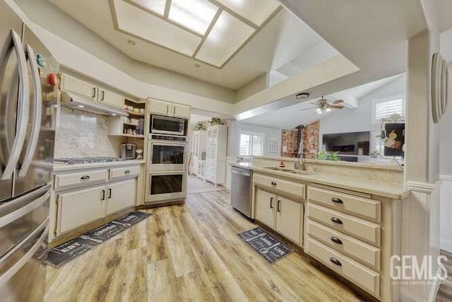 kitchen with tasteful backsplash, cream cabinets, vaulted ceiling, appliances with stainless steel finishes, and light wood-type flooring