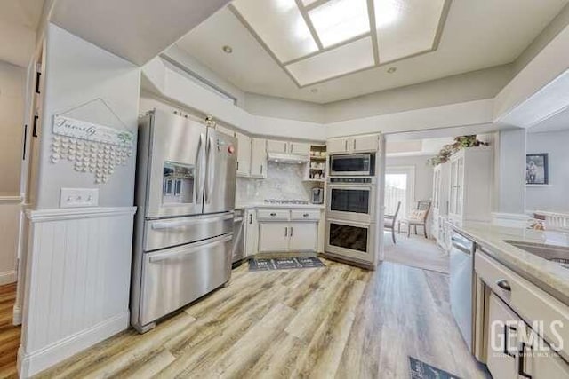 kitchen with appliances with stainless steel finishes, light wood-type flooring, and backsplash