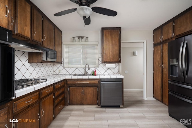 kitchen with a sink, tile countertops, appliances with stainless steel finishes, decorative backsplash, and dark brown cabinets