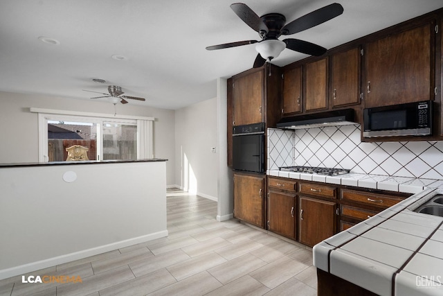 kitchen with tile countertops, oven, decorative backsplash, white gas stovetop, and under cabinet range hood