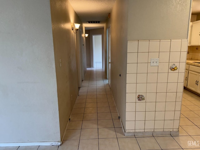 hallway with light tile patterned flooring, tile walls, and a textured ceiling