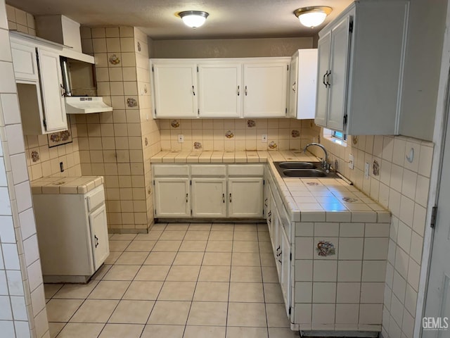 kitchen featuring sink, white cabinetry, light tile patterned floors, tile counters, and backsplash