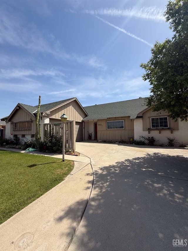 ranch-style home with a garage, driveway, a front yard, and roof with shingles