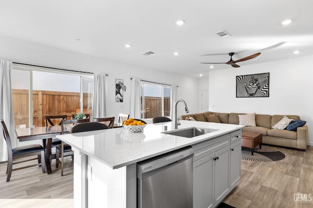 kitchen with stainless steel dishwasher, light stone countertops, sink, and a center island with sink